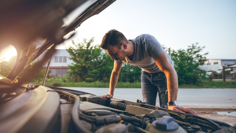Young handsome caucasian man looking under car hood.
