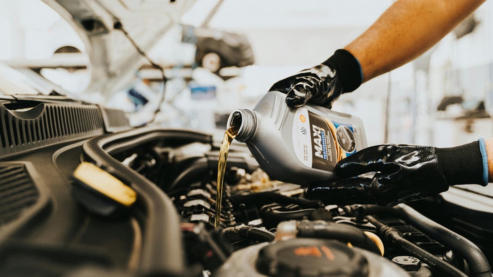 gloved mechanic pouring engine oil