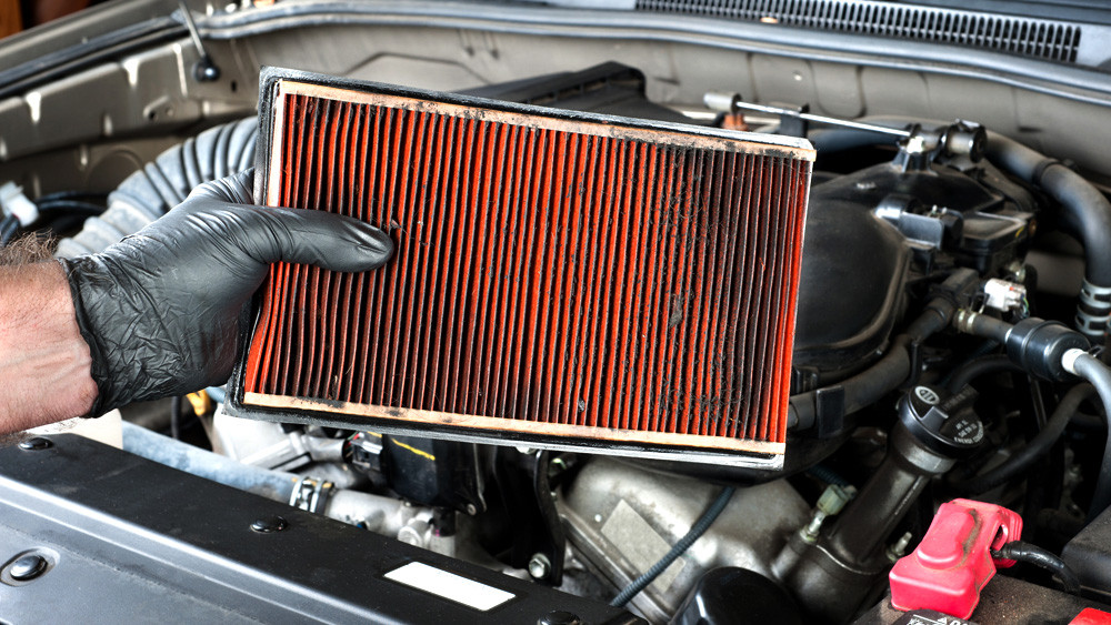 gloved hand holding a dirty air filter over engine bay
