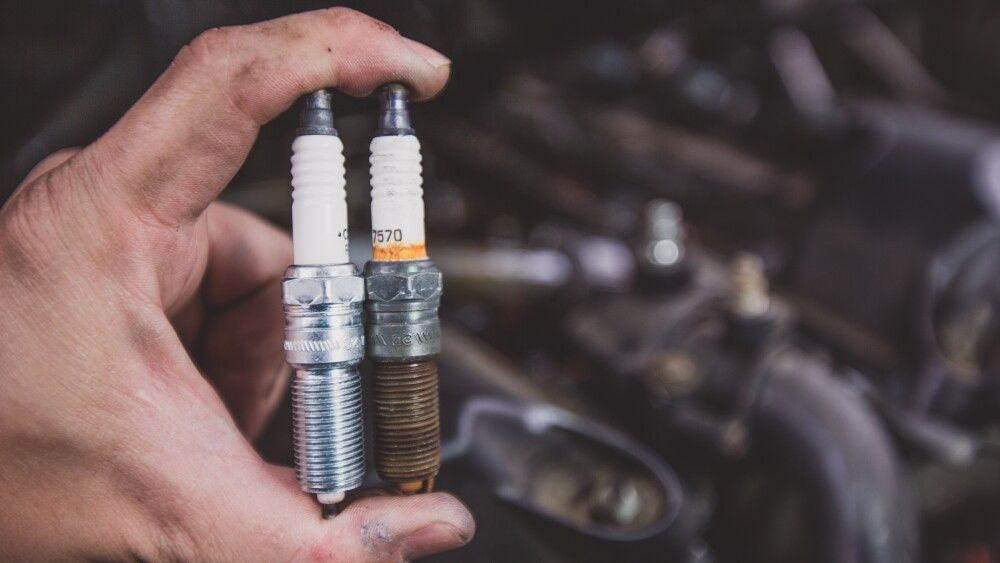 Holding old and new car spark plugs on engine