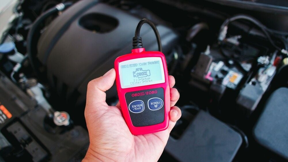 OBD2 or OBD scanner in a auto mechanic hand for engine system analysis with engine compartment blurred on background , Car maintenance service concept