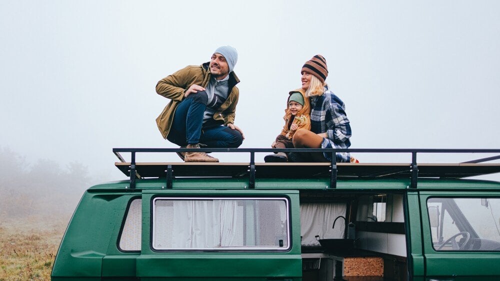 Smiling father, mother and their little daughter having fun while exploring nature with their van.