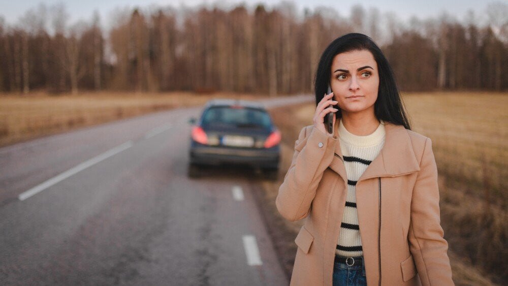 Young woman is stranded on the road because her car broke down. She is phoning for help.