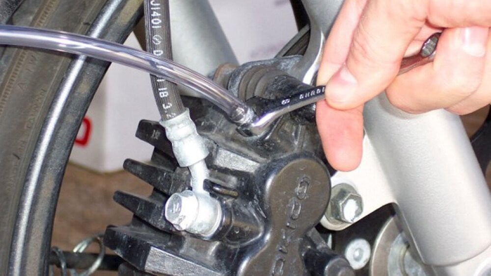 Technician twisting the bleeder screw on a brake caliper to bleed the system