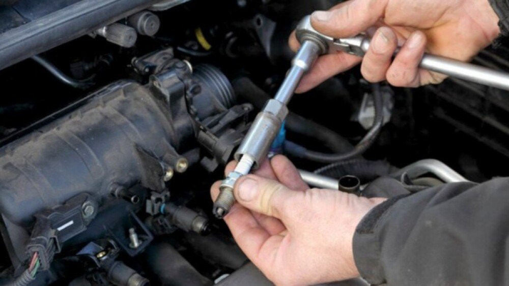 Person working through a spark plug replacement, holding a socket and ratchet with a removed spark plug